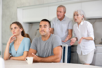 Girl and guy are sitting in kitchen and do not listen to their father and mother