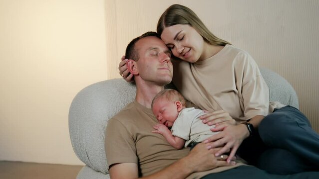 Happiness portrait. Caucasian couple sitting on the sofa with a tiny newborn boy sleeping on dad's chest.