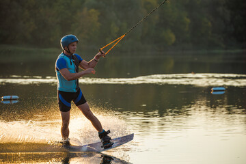 An athlete does a trick on the water. A rider jumps on a wakeboard against a background of a green...