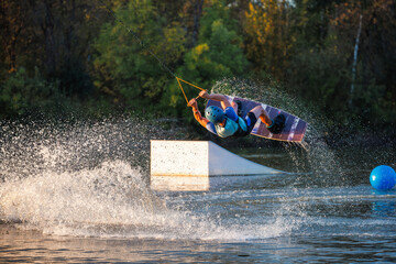 An athlete does a trick from a springboard. A rider jumps on a wakeboard against a background of a...