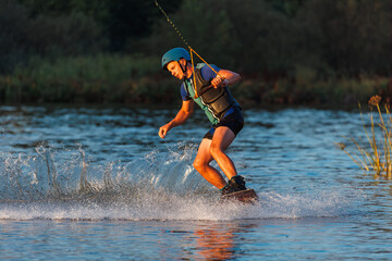 An athlete performs a trick on the water. Park at sunset. Wakeboard rider