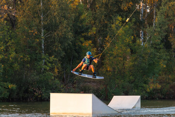 An athlete jumps from a springboard. Wakeboard park at sunset. A man performs a trick on a board