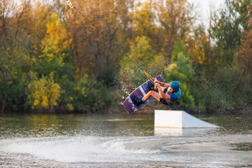 An athlete jumps from a springboard. Wakeboard park at sunset. A man performs a trick on a board