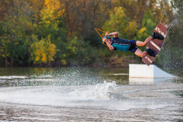 An athlete jumps from a springboard. Wakeboard park at sunset. A man performs a trick on a board