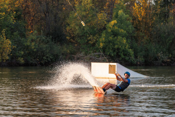 An athlete performs a trick on the water. Park at sunset. Wakeboard rider