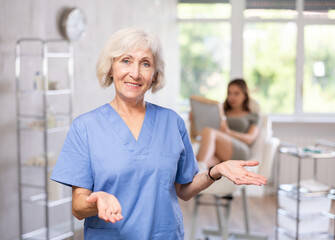 Obraz premium Positive confident female doctor standing while young patient laying on treatment chair and looking in mirror.