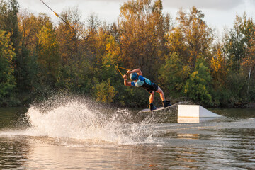 An athlete jumps from a springboard. Wakeboard park at sunset. A man performs a trick on a board