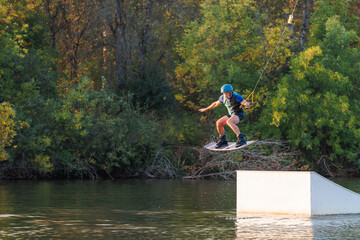 An athlete jumps from a springboard. Wakeboard park at sunset. A man performs a trick on a board