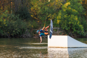 An athlete jumps from a springboard. Wakeboard park at sunset. A man performs a trick on a board