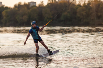 An athlete jumps over the water. Wakeboard park at sunset. Rider performs a trick on the board