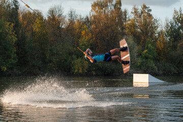 An athlete jumps from a springboard. Wakeboard park at sunset. A man performs a trick on a board