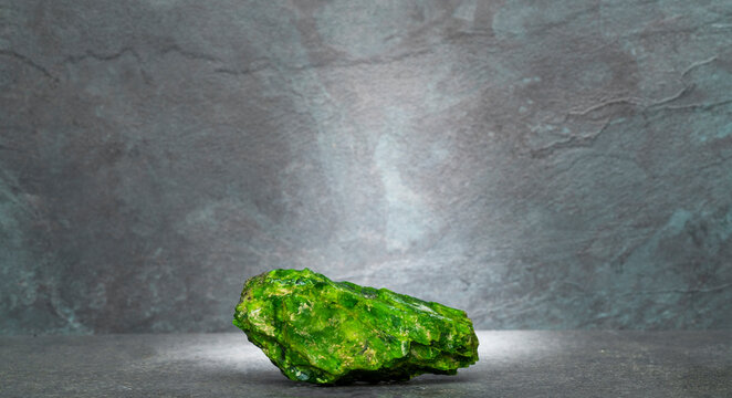 green chrome diopside stone on a dark gray background for a product presentation podium. natural green stones on a gray background for the presentation of perfumes, jewelry, cosmetics, medicines.