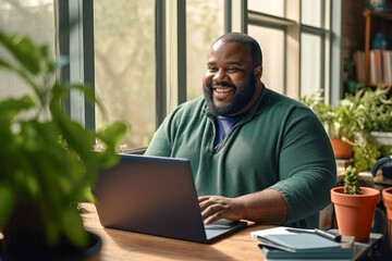 Portrait of an overweight African American man working from home on a laptop computer - obrazy, fototapety, plakaty