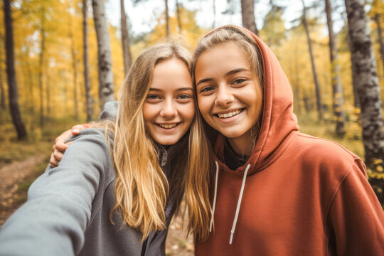 Two teenage girls taking selfie in forest in autumn. Friends hiking in autumn forest and taking photo of themselves
