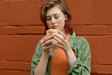 Street food concept. Attractive gen z young woman eating burger outside. 