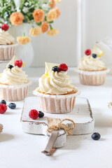 Lemon cupcakes with berries on the white wooden background.