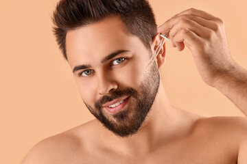 Handsome man applying cosmetic serum onto face on beige background, closeup