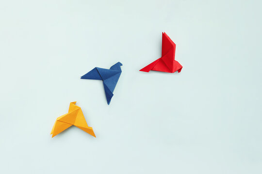 three paper origami pigeons yellow, blue and red on light blue background