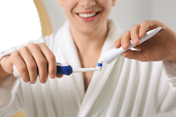 Man squeezing toothpaste from tube onto electric toothbrush in bathroom, closeup