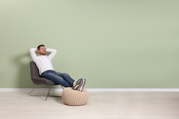 Happy man sitting in armchair near light green wall indoors, space for text