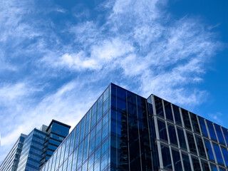 Angled view of a large, window covered building corner against a blue, cloud filled sky