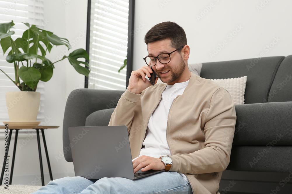 Poster man talking on smartphone while working with laptop at home