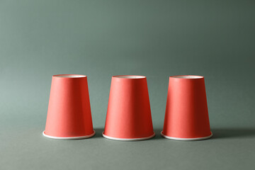 Three red cups on pale olive background. Thimblerig game