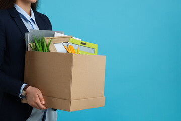Unemployed woman with box of personal office belongings on light blue background, closeup. Space for text