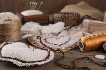 Pieces of burlap fabric with different stitches and needle with thread on wooden table, closeup