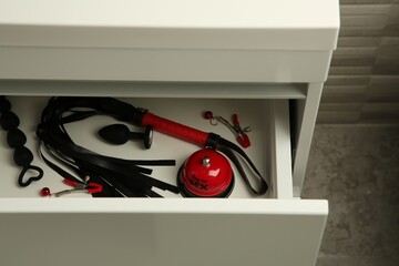 Whip, nipple clamps, bell and anal plug in drawer indoors. Sex toys