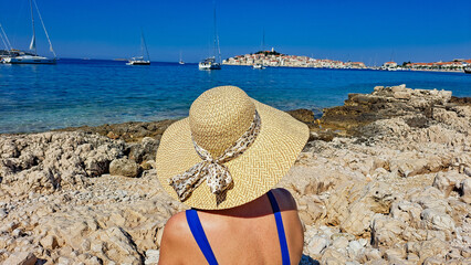 Kobieta w kapeluszu na plaży wpatruje wię w morze