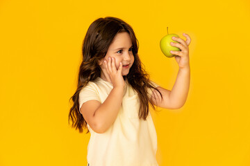 Cute little girl holding green apple isolated on yellow background. Proper nutrition. Child health. Vegetaridism. High quality photo