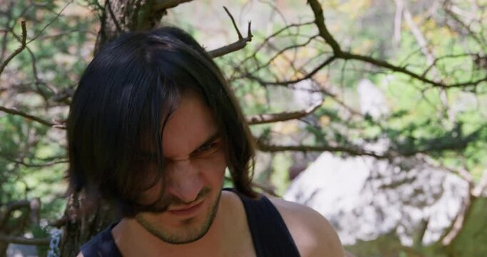 Long-haired man tries hard to break free from iron chains. Bearded male victim moving body and hands after getting tied in countryside closeup