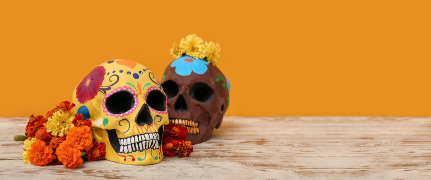 Painted human skulls for Mexico's Day of the Dead (El Dia de Muertos) and flowers on table against orange background with space for text