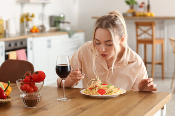 Young woman eating tasty pasta in kitchen