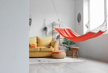 Interior of stylish living room with red hammock and yellow sofa, view from hallway