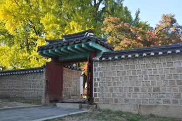 Traditional Korean Hanok Village stone wall with old wooden door and big trees in the afternoon in Seoul, South Korea