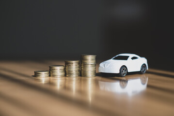 Money and a white miniature car drives are placed on a wooden table, showing saving money to buy a...