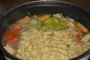 Photo of a pot of noodles being cooked with some vegetable toppings