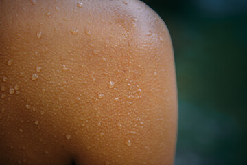 Close-up female tanned shoulder, showing skin detail with water droplets and goose bumps. Part of...