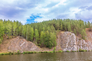 Pine trees and rocks on the river shore with fall foliage around