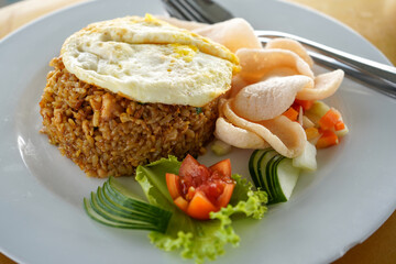 Javanese fried rice consisting of rice, fried eggs, pickled cucumber, vegetables on a white plate with cutlery which is a menu in a cafe and restaurant.