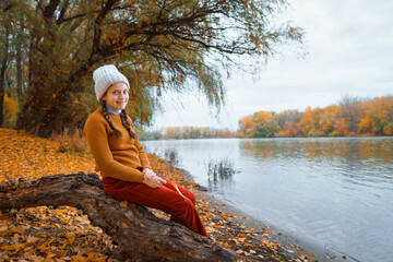 a young teenage girl posing in an autumn forest, sitting on a tree by the river bank, beautiful nature and bright yellow leaves