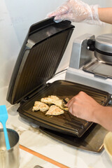 Chef frying chicken meat in butter in electric griller