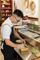 Vietnamese man chef in uniform holding fresh baked belgian waffles with chicken and putting them in paper box for take away