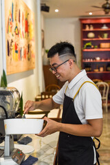 Fototapeta premium Vietnamese man chef in uniform holding spoon and bowl with liquid dough for belgian waffles