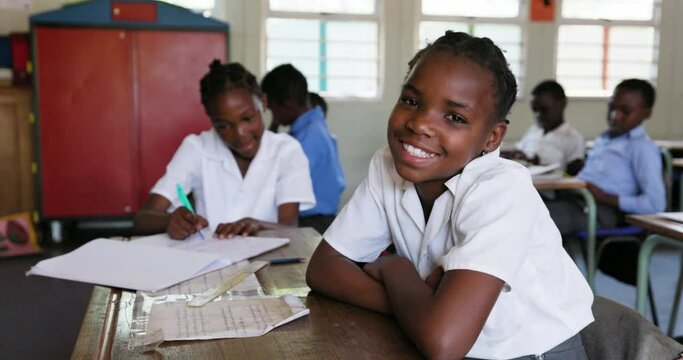 Close-up. Black African school girl smiling at camera sitting at a desk in a classroom in Africa