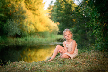 Portrait of a little blonde girl barefoot on the background of the river
