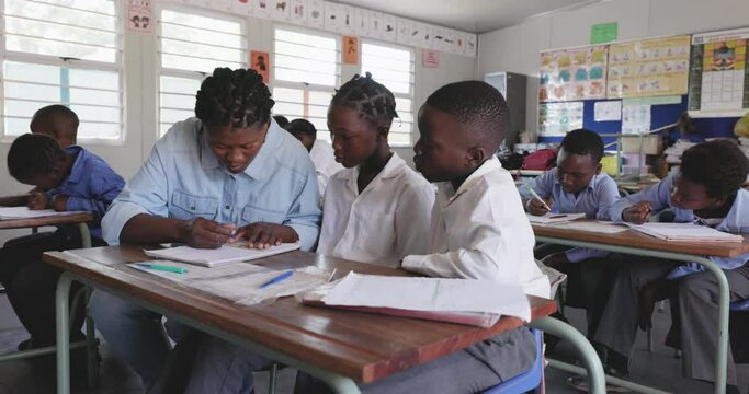 Close-up. Black African female teacher sitting and assisting African children with a drawing at their desk in a classroom in Africa