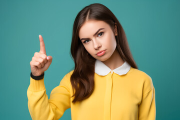Serious brunette schoolgirl pointing up with index finger on blue background. Girl raises finger up, says: Attention please